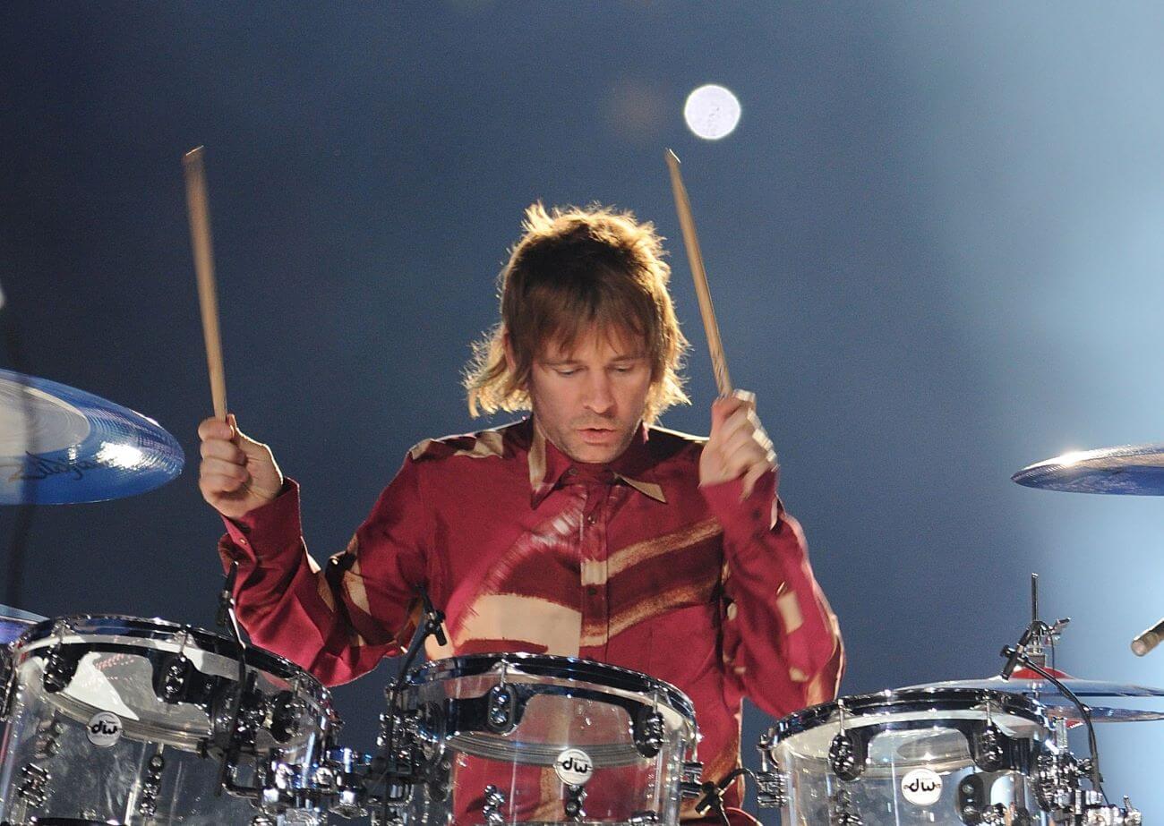 Zak Starkey wears a red shirt and plays drums.