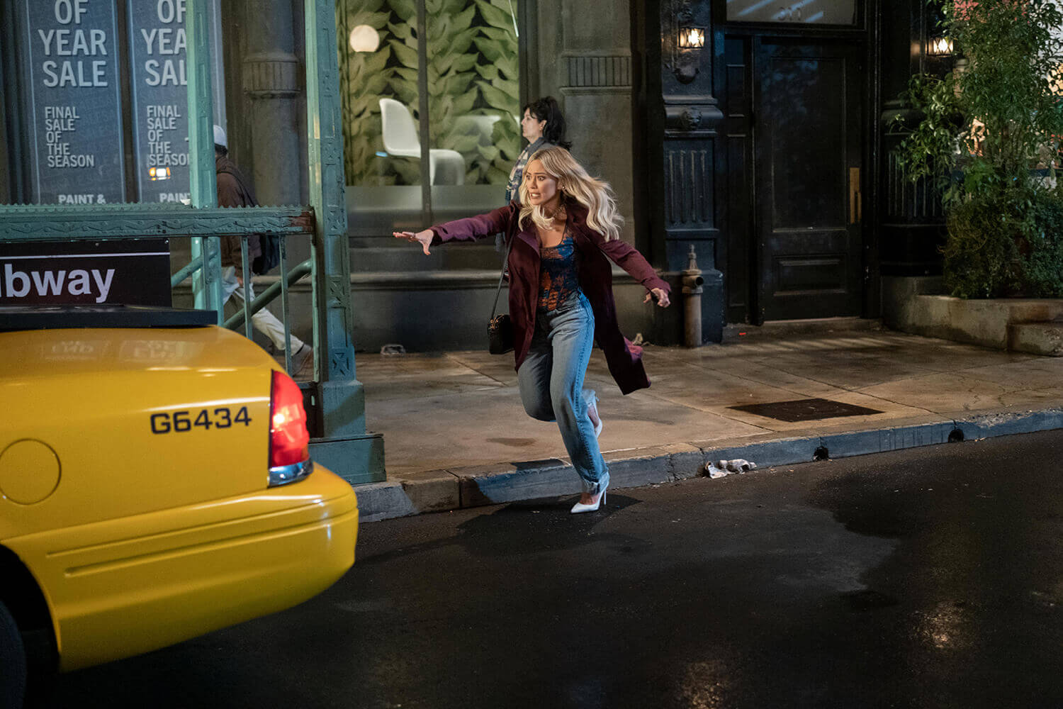 How I Met Your Father: Hilary Duff as Sophie chasing a taxi that drives away with her photo on the back hood.