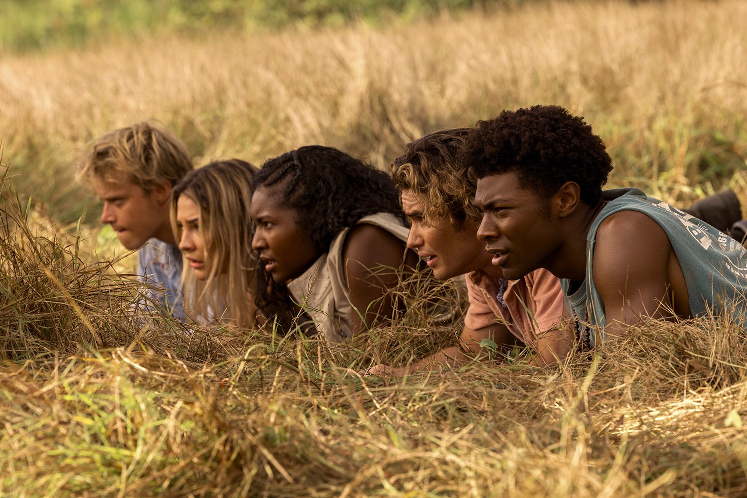 Outer Banks Season 3 photo shows Rudy Pankow as JJ, Madelyn Cline as Sarah Cameron, Carlacia Grant as Cleo, Chase Stokes as John B, and Jonathan Daviss as Pope hiding in the grass