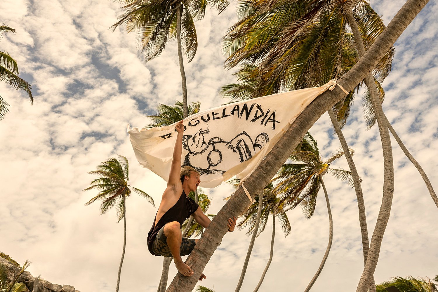 Rudy Pankow as JJ hanging on a tree with a Poguelandia sign in the Outer Banks Season 3 trailer