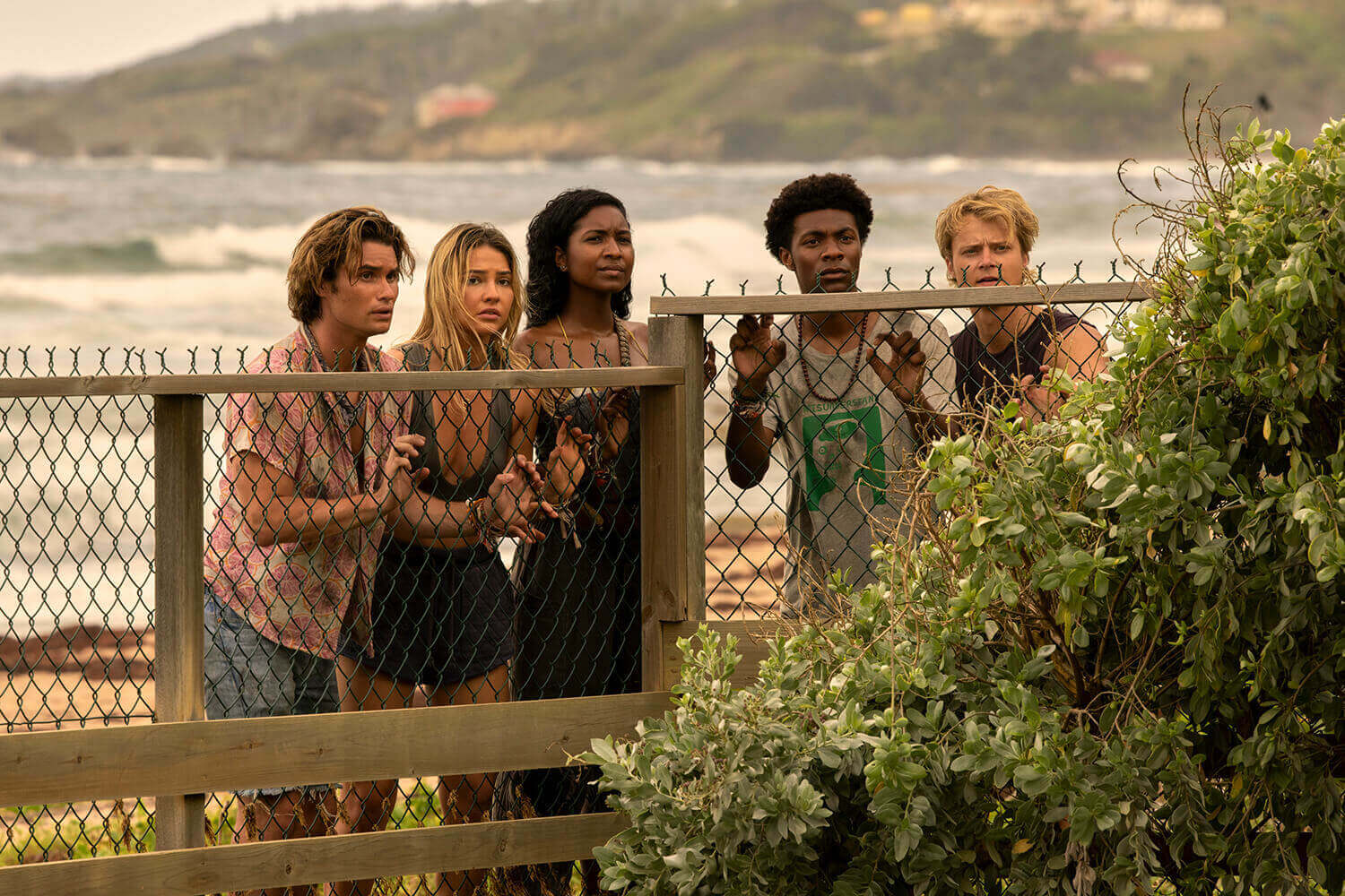 Outer Banks cast members Chase Stokes as John B, Madelyn Cline as Sarah, Carlacia Grant as Cleo, Jonathan Daviss as Pope, and Rudy Pankow as JJ in looking over a wooden fence