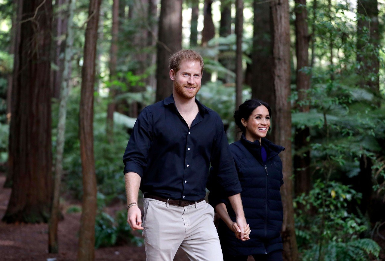 Prince Harry and Meghan Markle hold hands while walking through the forest.