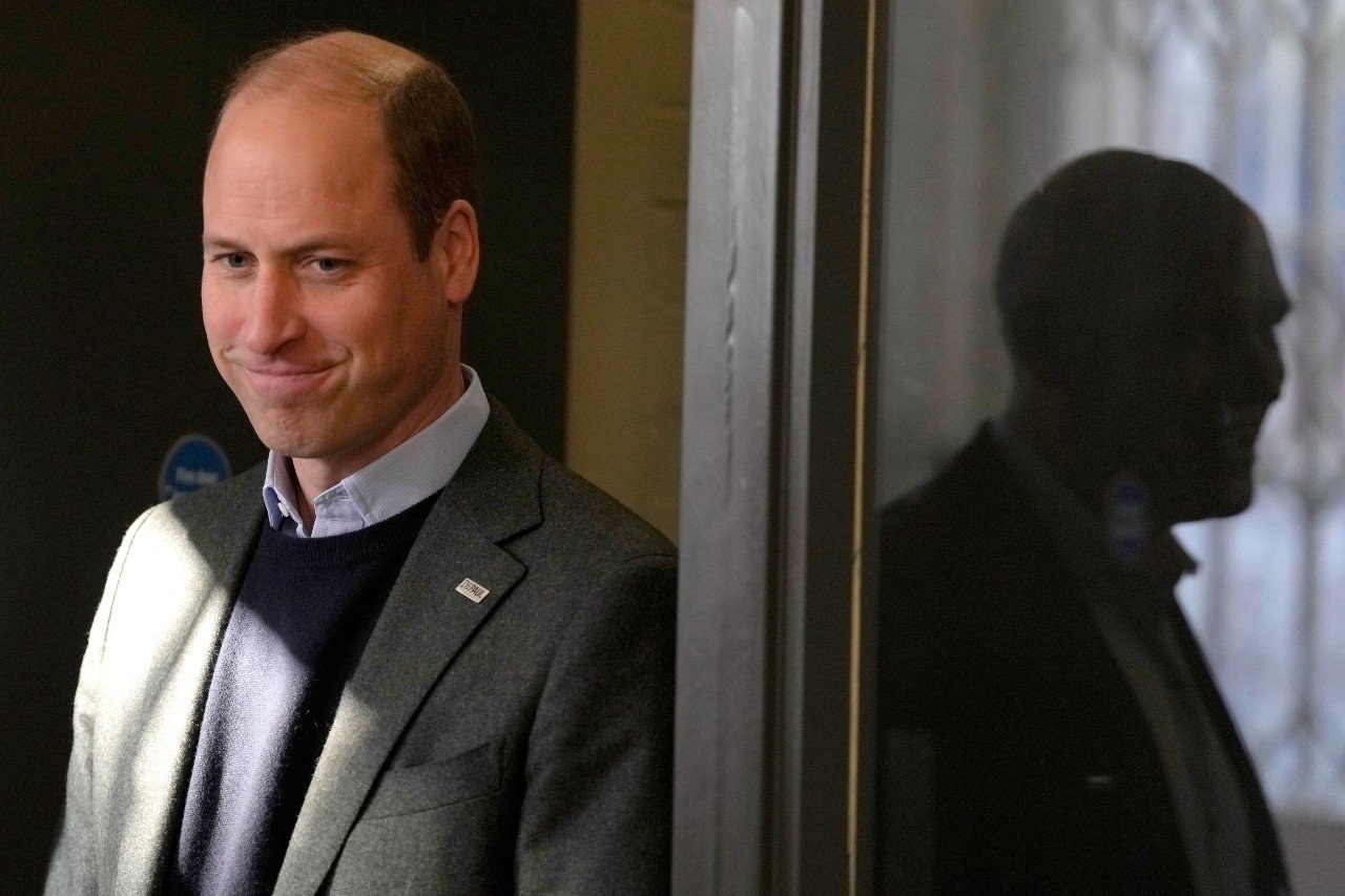 Prince William smiles while standing in a doorway.