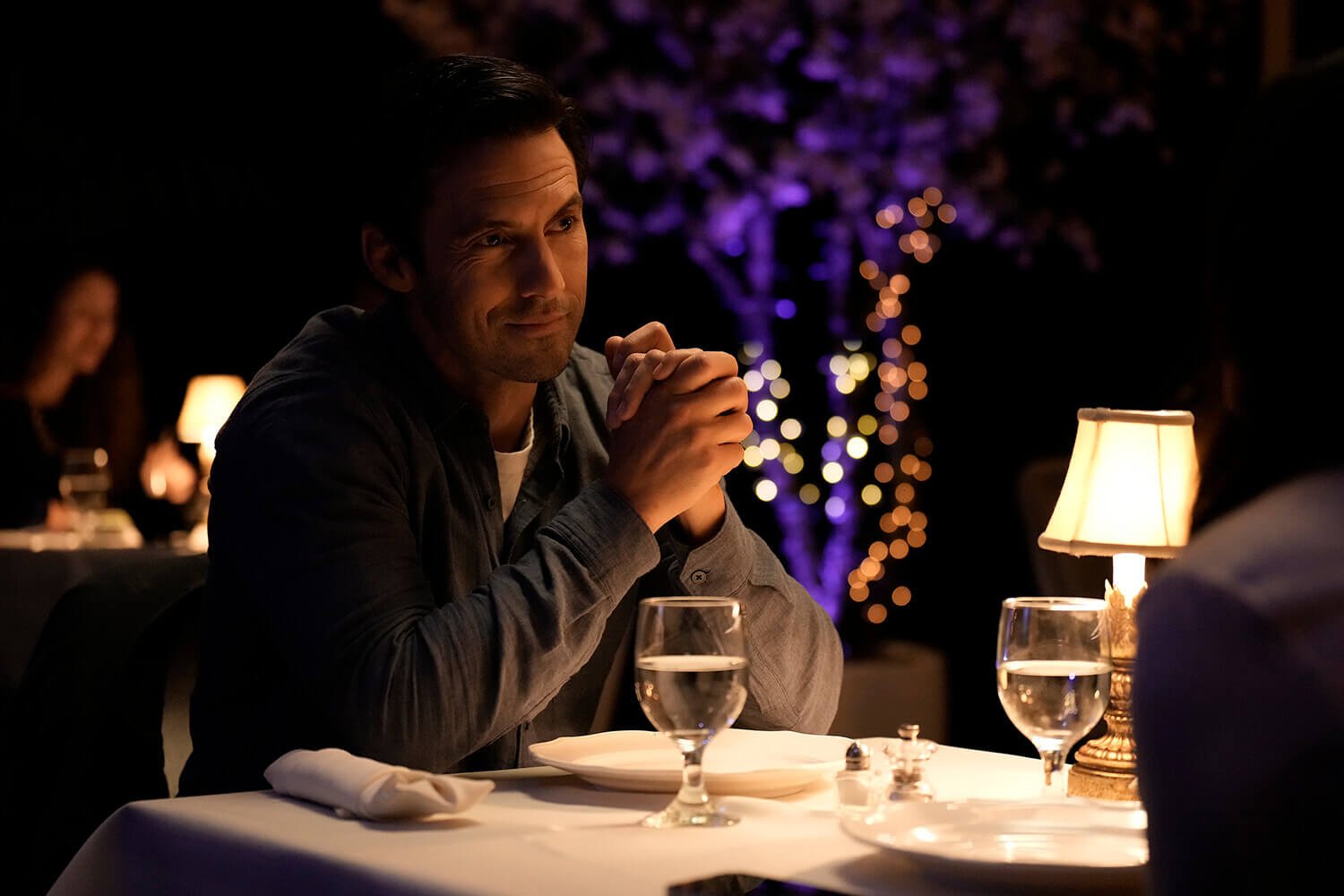 Milo Ventimiglia as Charlie sitting at a restaurant dinner table in The Company You Keep