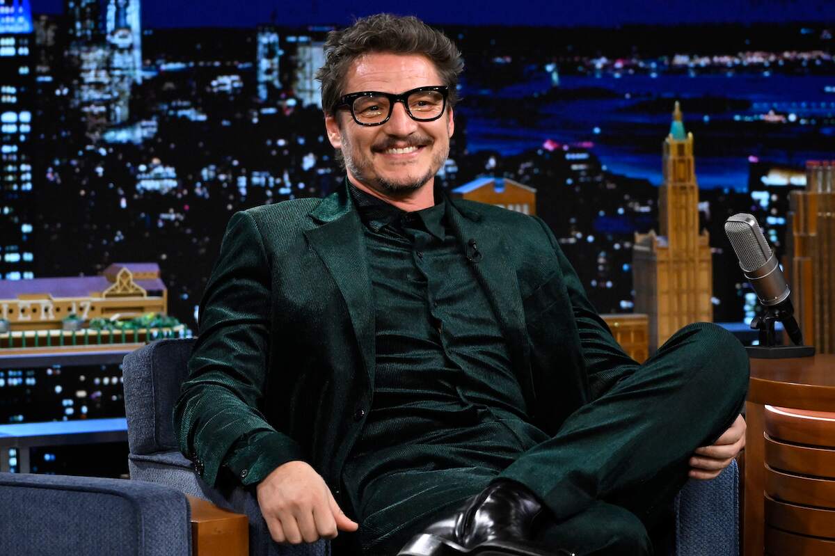 Actor Pedro Pascal smiles during an interview while wearing a black suit
