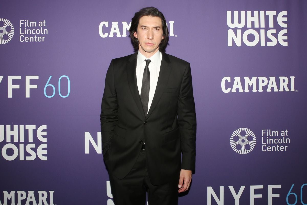 Adam Driver poses in front of a purple backdrop featuring the NYFF logo.