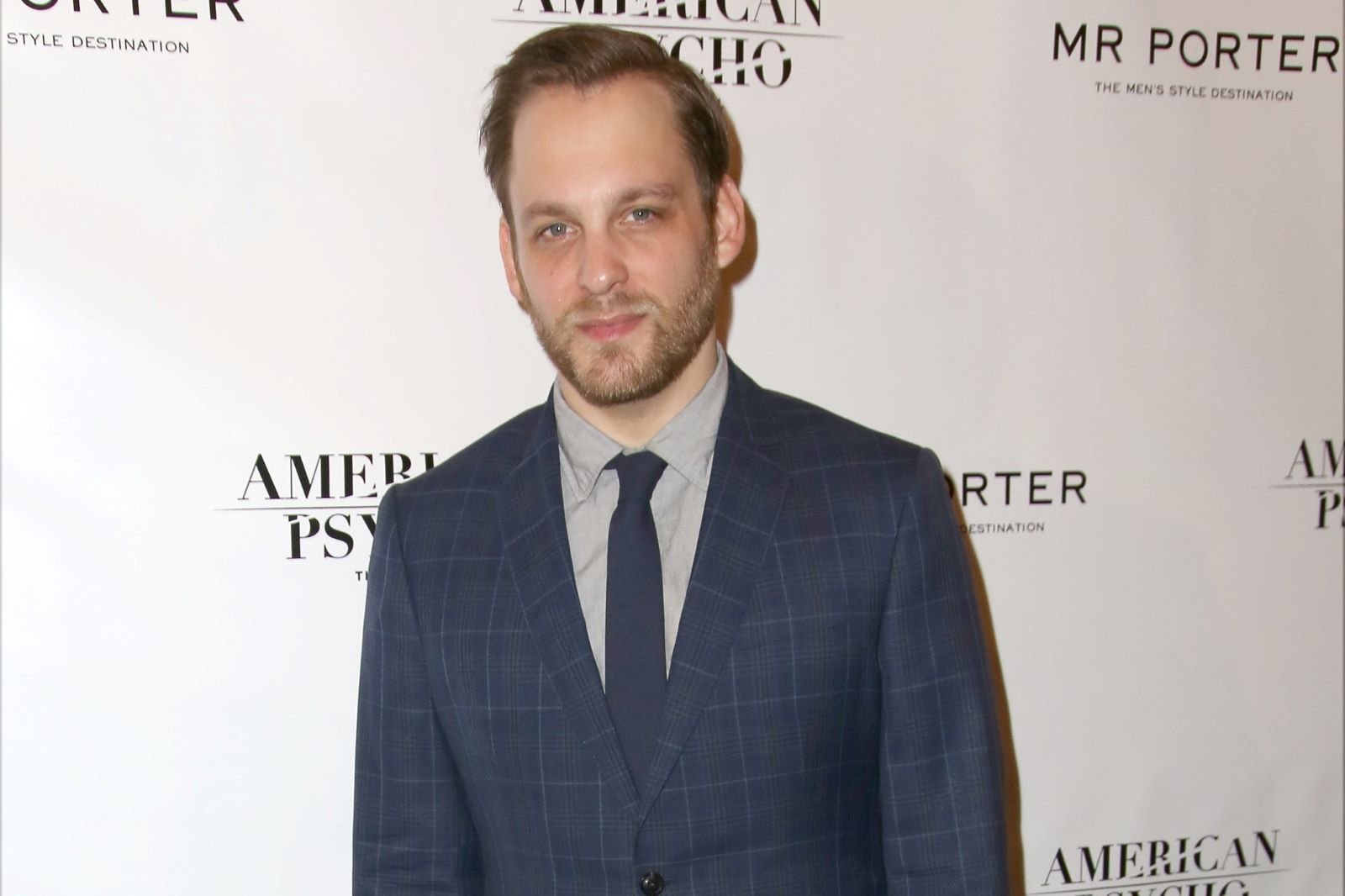 Theo Stockman, who plays Ezra Fisher in 'Alaska Daily' on ABC, wears a dark blue suit over a light gray button-up shirt and dark blue tie.
