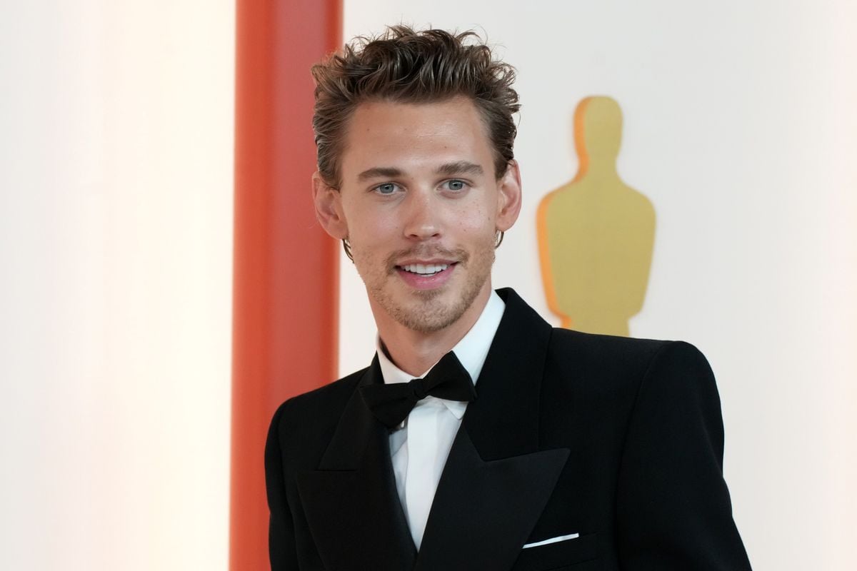 Austin Butler poses in front of a backdrop featuring an image of the Oscars statuette.
