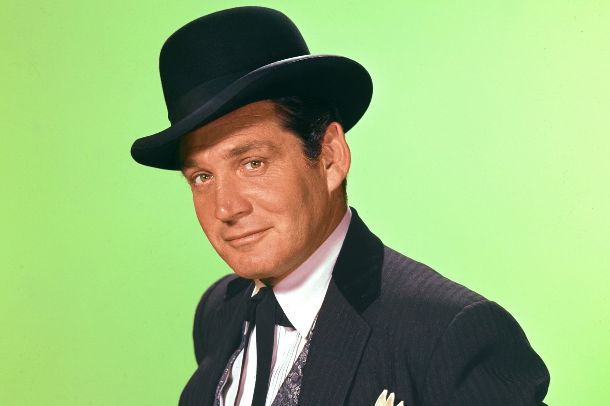 'Bat Masterson' Gene Barry as Bat Masterson smiling in front of a green background.