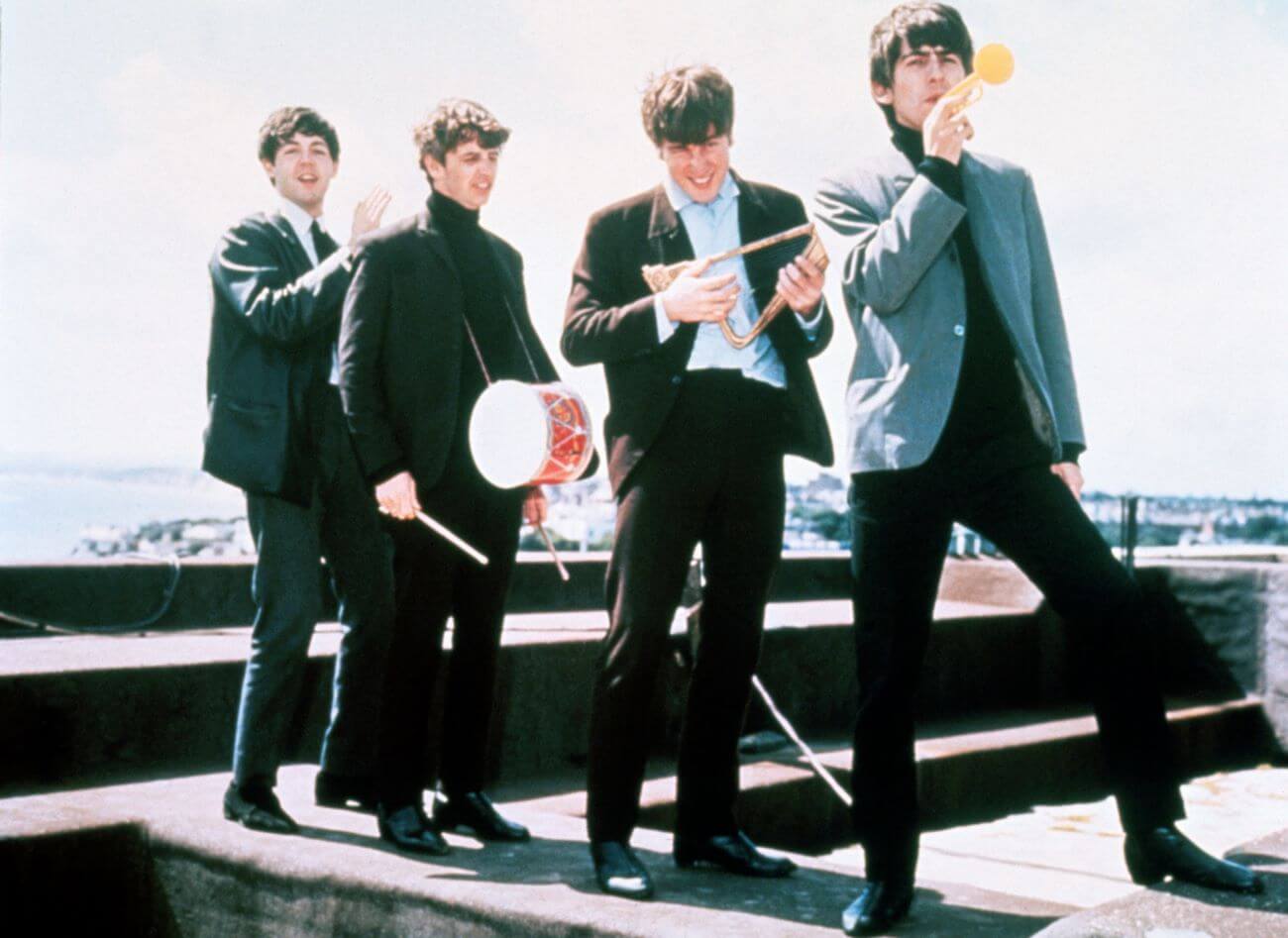 The Beatles stand on a rooftop with small instruments.