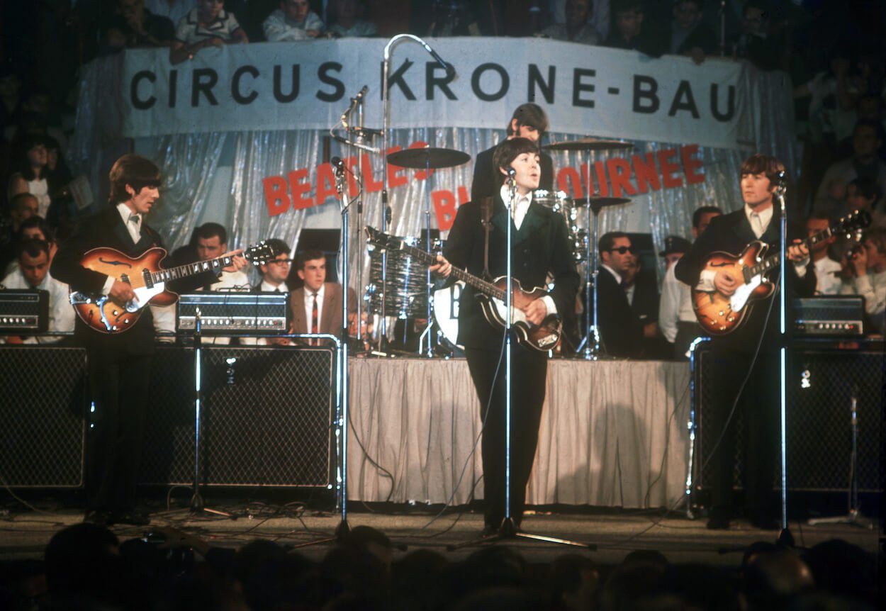 George Harrison (from left), Paul McCartney, and John Lennon (with Ringo Starr in the background) wear black suits while playing in Germany in 1966.