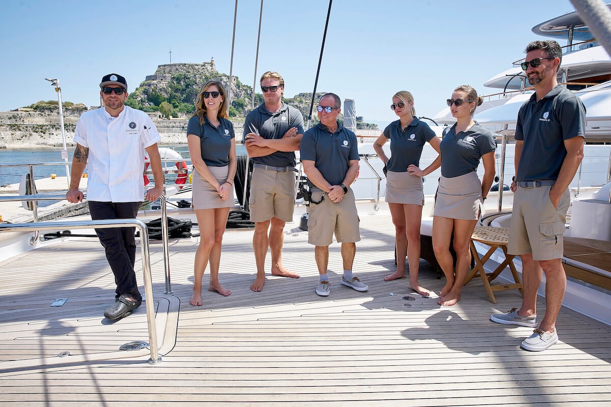 Cast members of 'Below Deck Sailing Yacht' standing outside in the sun on a boardwalk