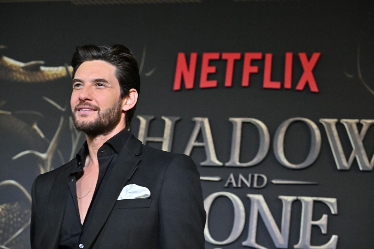 Ben Barnes poses for a photo in front of the "Shadow and Bone" logo.