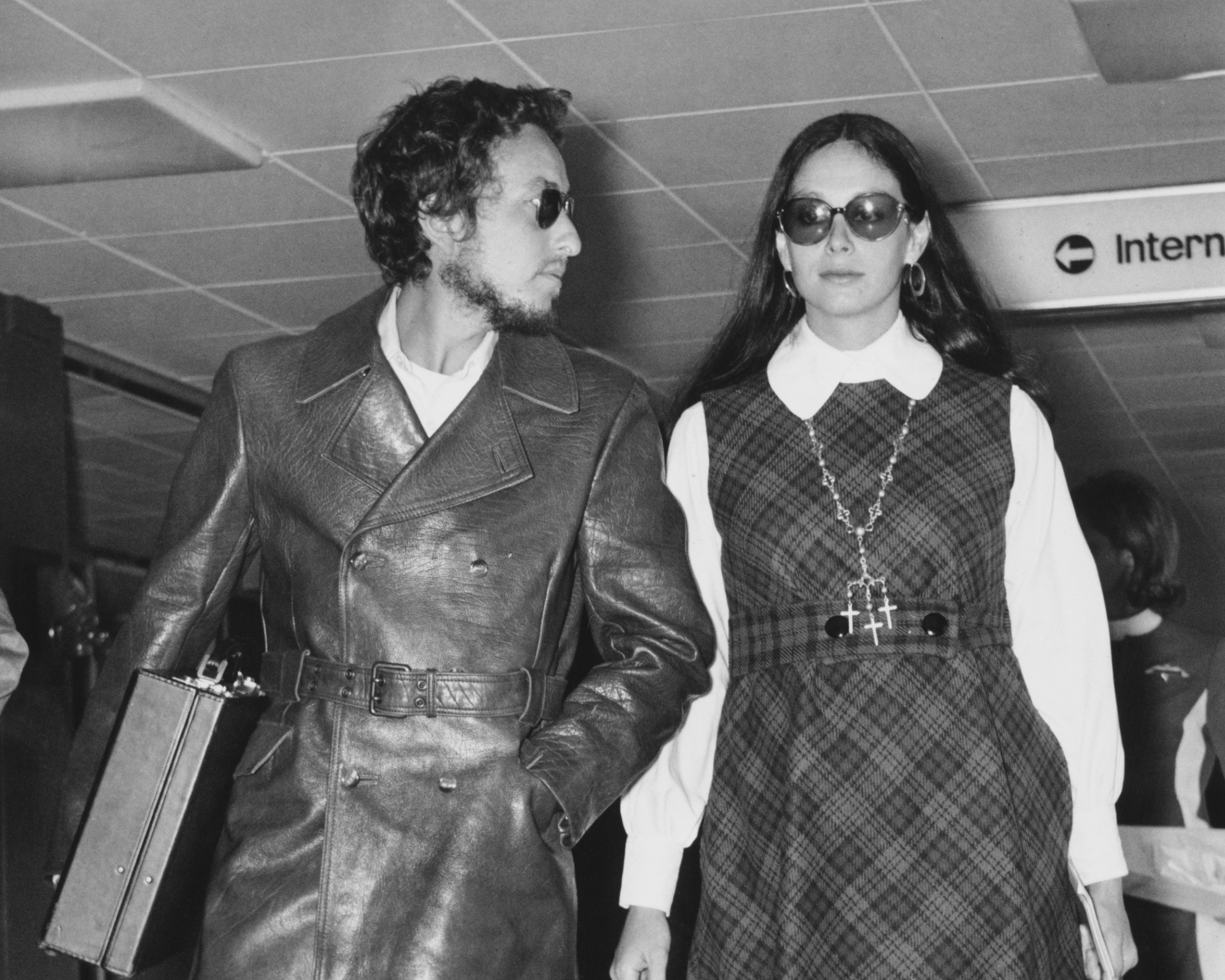 A black and white picture of Bob Dylan and Sara Dylan walking through an airport wearing sunglasses.