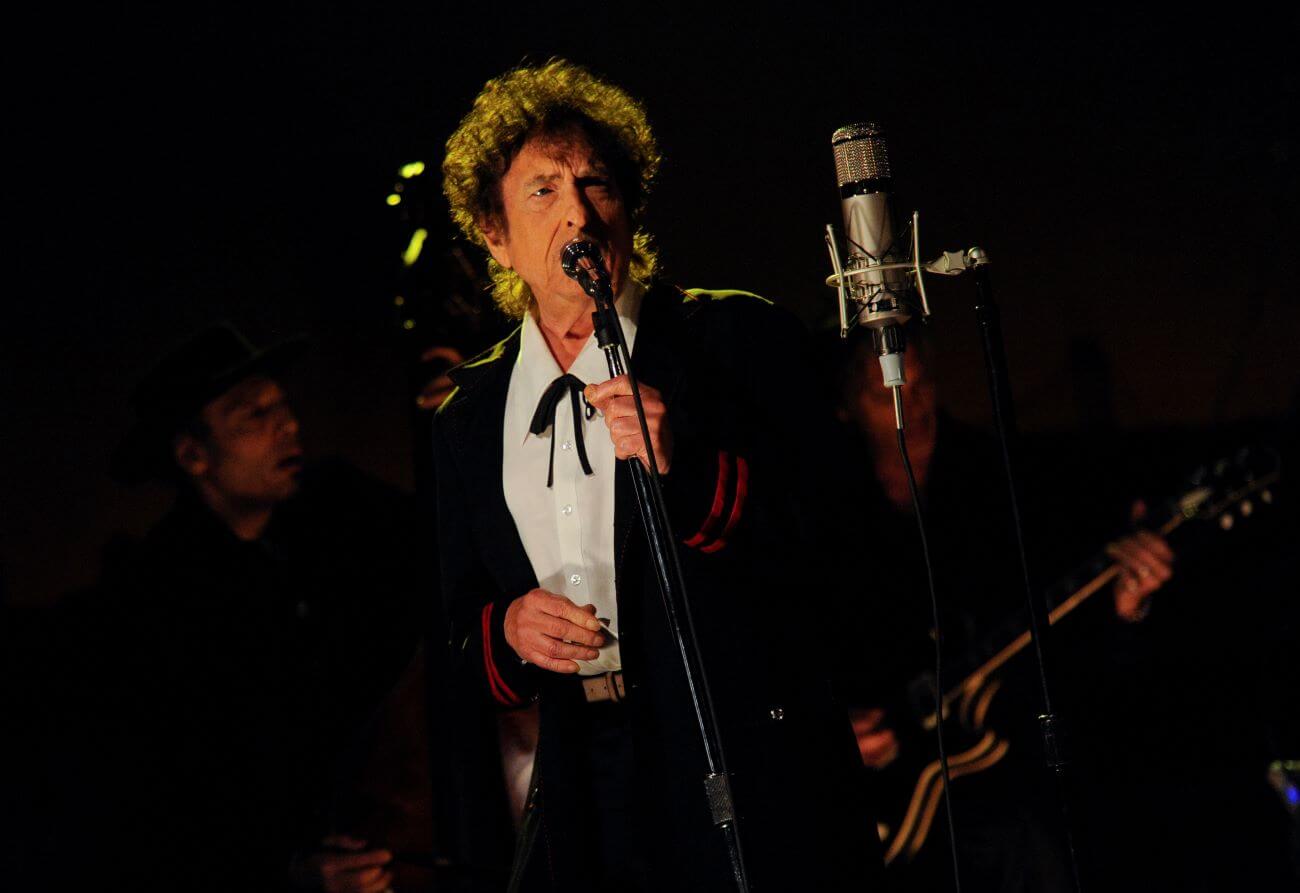 Bob Dylan sings into a microphone and wears a bow tie.