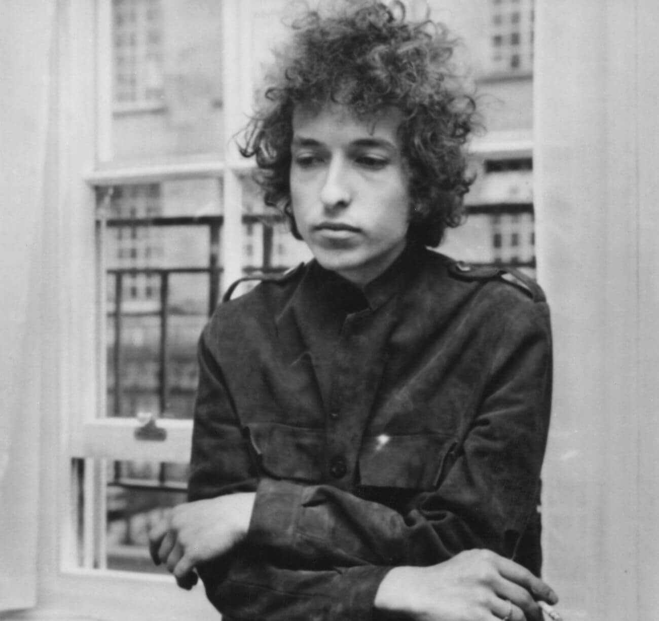 A black and white picture of Bob Dylan leaning against a window.