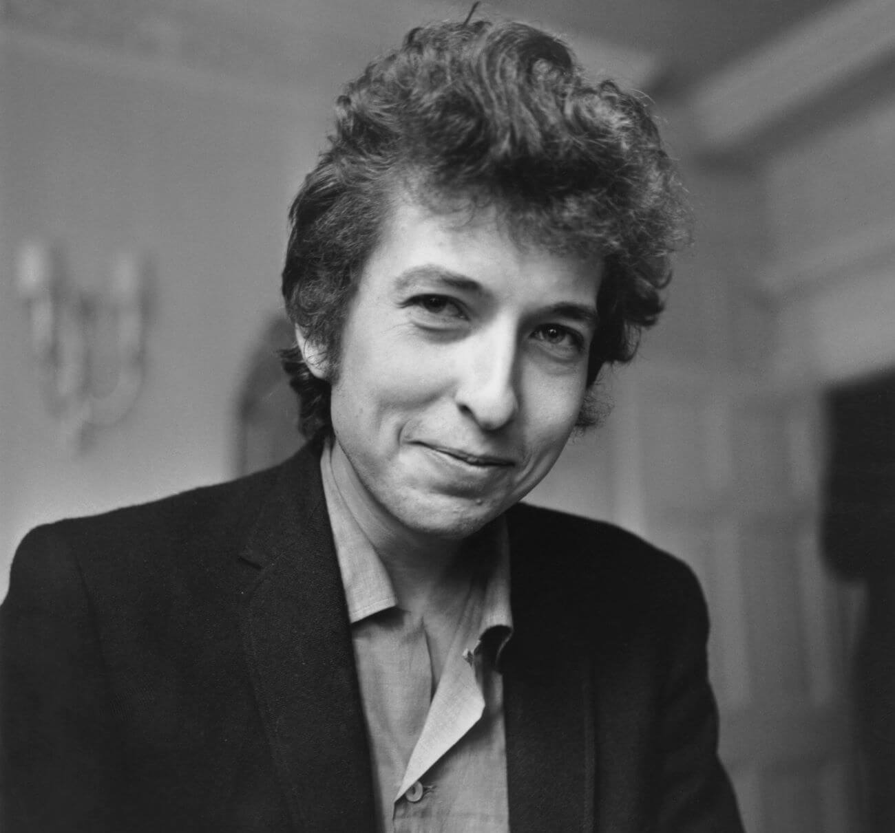 A black and white picture of Bob Dylan wearing a suit jacket and smiling.