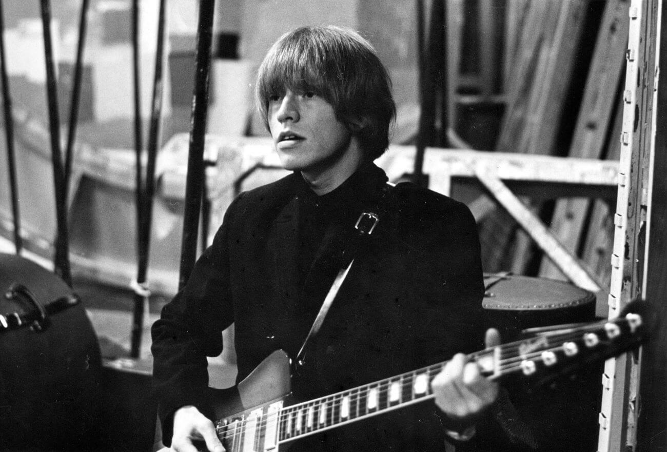 A black and white picture of Brian Jones holding a guitar.