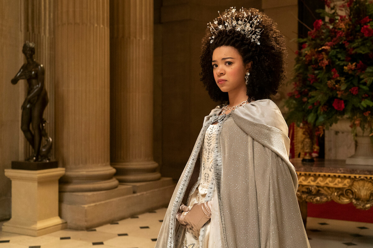 India Amarteifio as Queen Charlotte standing in a crown and a cape in 'Queen Charlotte: A Bridgerton Story'