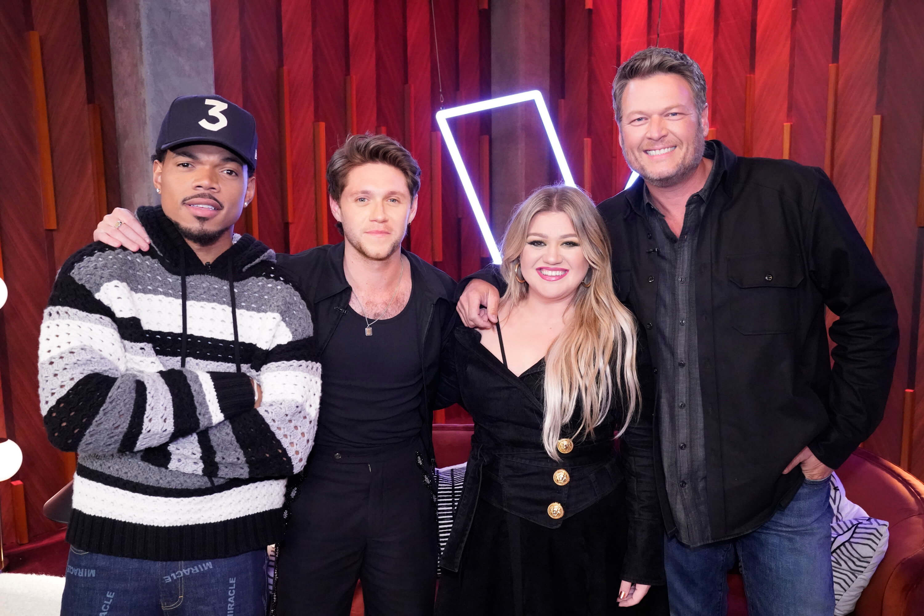'The Voice' coaches Chance the Rapper, Niall Horan, Kelly Clarkson, and Blake Shelton smile together in front of a red background