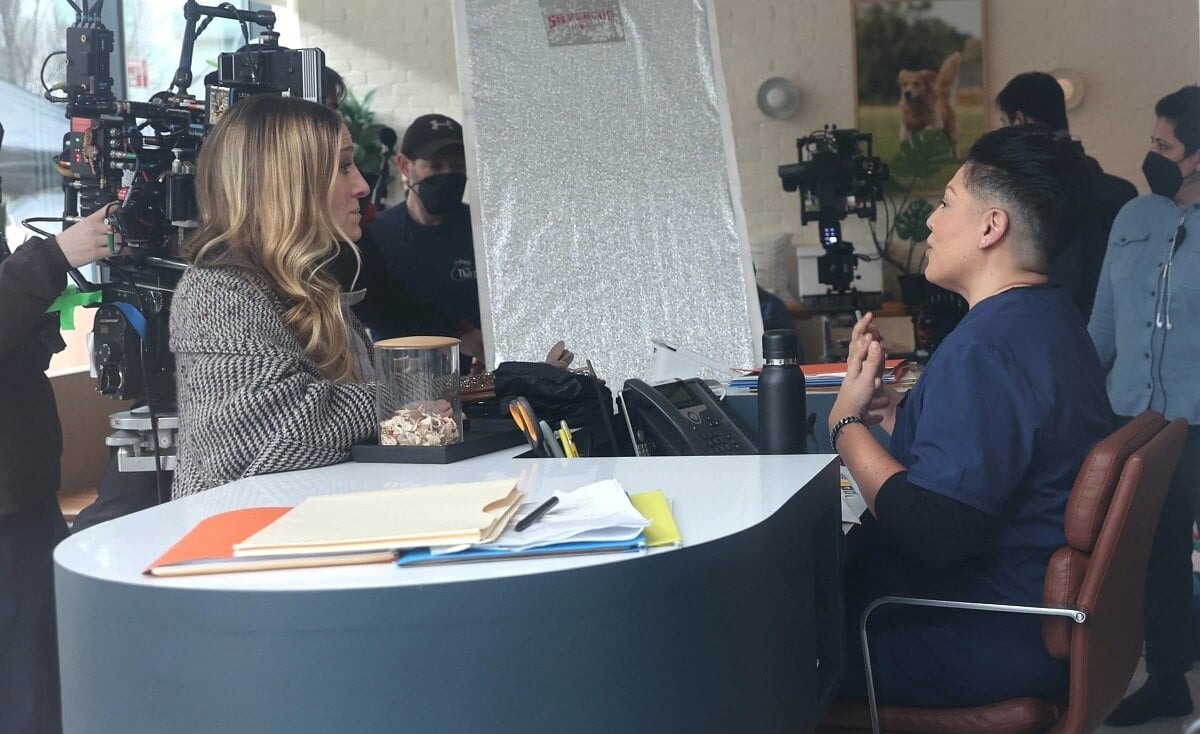 Sarah Jessica Parker as Carrie Bradshaw and Sara Ramirez Che Diaz sit across from each other at a desk during the filming of 'And Just Like That...' season 2