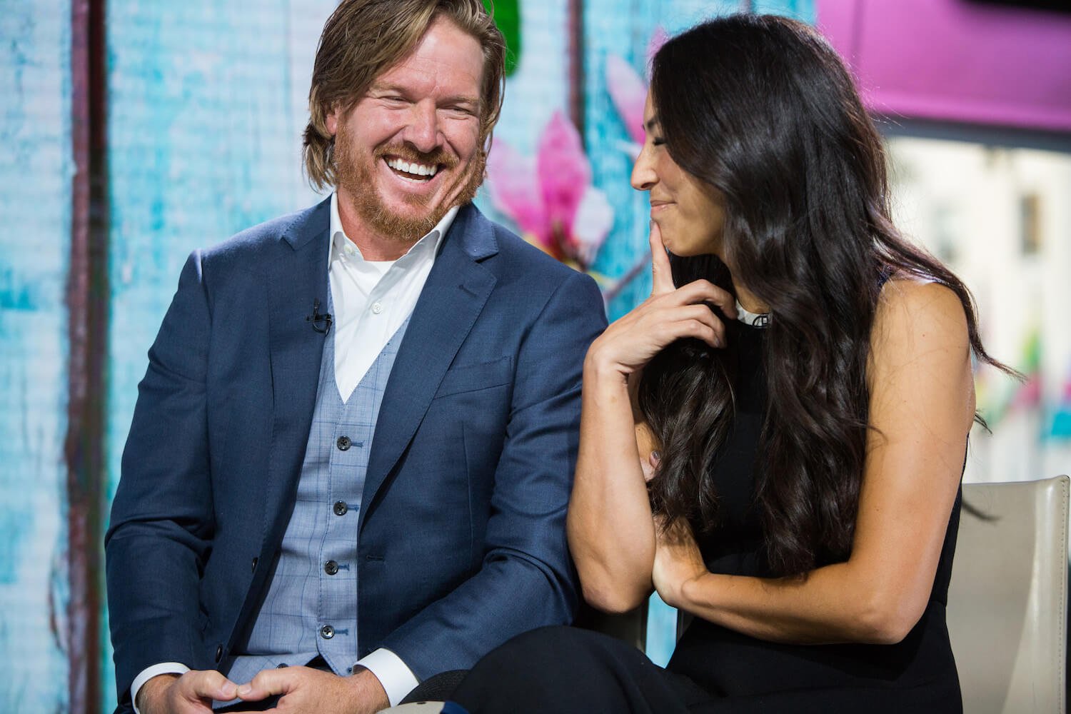 Chip and Joanna Gaines from 'Fixer Upper' sitting next to each other laughing during an interview