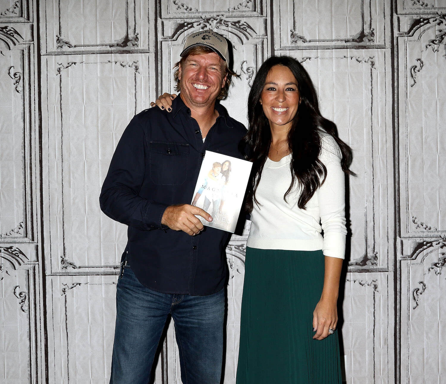 Chip and Joanna Gaines from 'Fixer Upper' smiling while holding their memoir about Magnolia