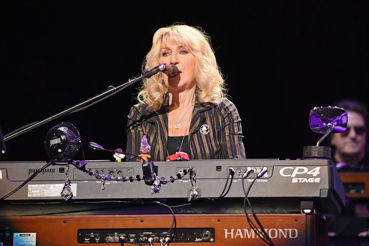 Christine McVie plays a keyboard and sings into a microphone.