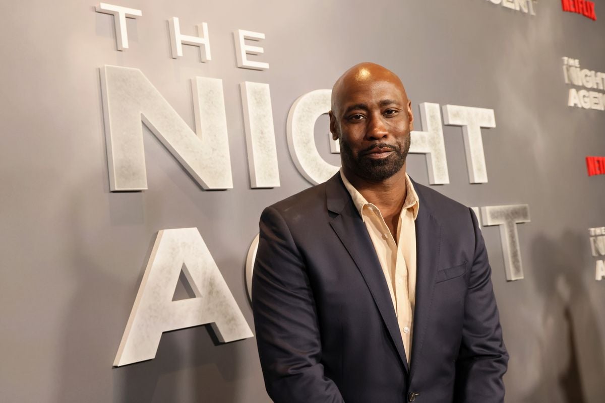 D.B. Woodside aposes for a photo in front of a backdrop featuring the logo for "The Night Agent"