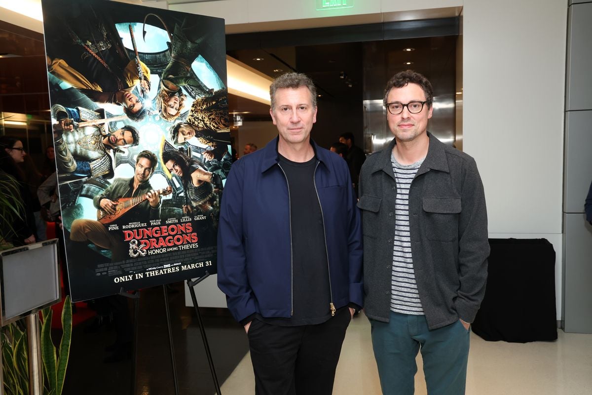 Jonathan Goldstein and John Francis Daley pose for a photo in front of a movie poster for “Dungeons & Dragons: Honor Among Thieves”