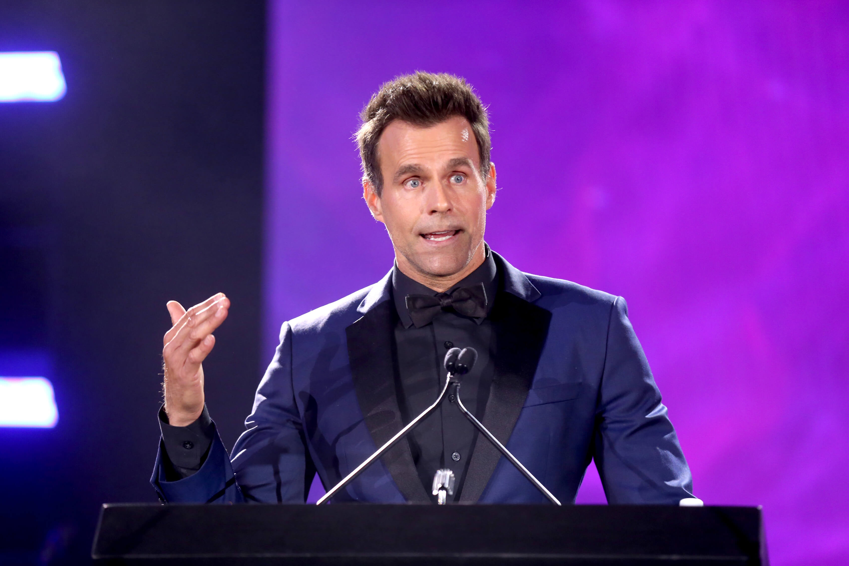 'General Hospital' star Cameron Mathison in a blue and black suit; speaking into a microphone podium.