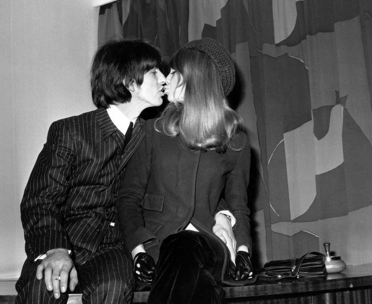 Beatles guitarist George Harrison (left) wears pinstriped suit as he kisses Pattie Boyd during a January 1966 press conference.