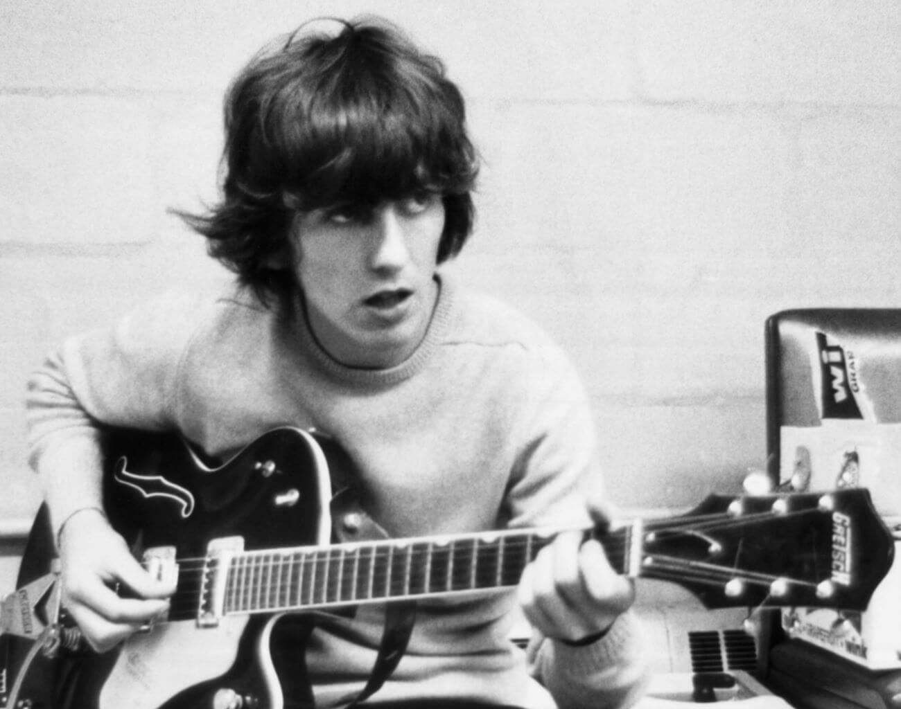 A black and white picture of George Harrison sitting with a guitar.