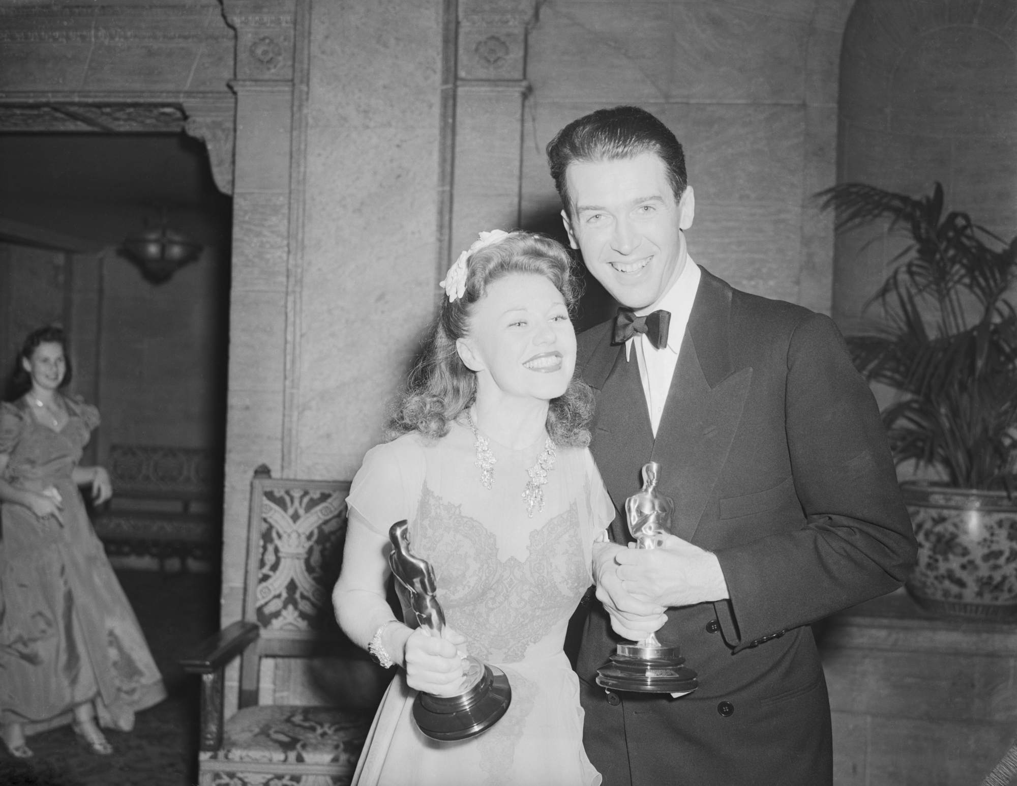 Ginger Rogers and 'The Philadelphia Story' actor Jimmy Stewart holding their Oscar statuettes in a black-and-white picture, smiling.