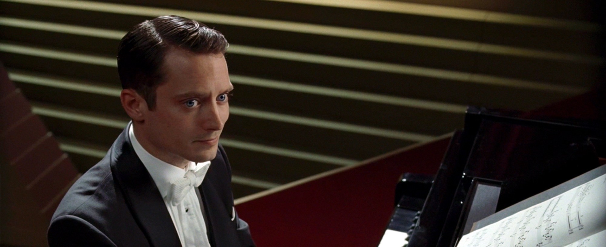 'Grand Piano' Elijah Wood as Tom Selznick sitting behind the piano, looking up.