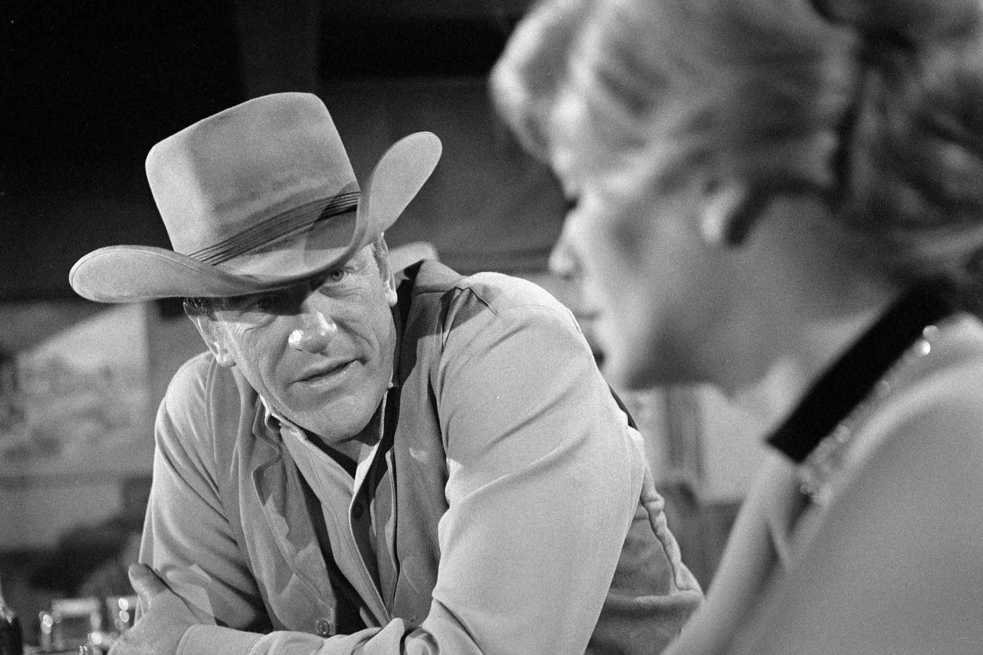 'Gunsmoke' James Arness as Matt Dillon and Betty Hutton as Molly McConnell look at one another, leaning on a table.