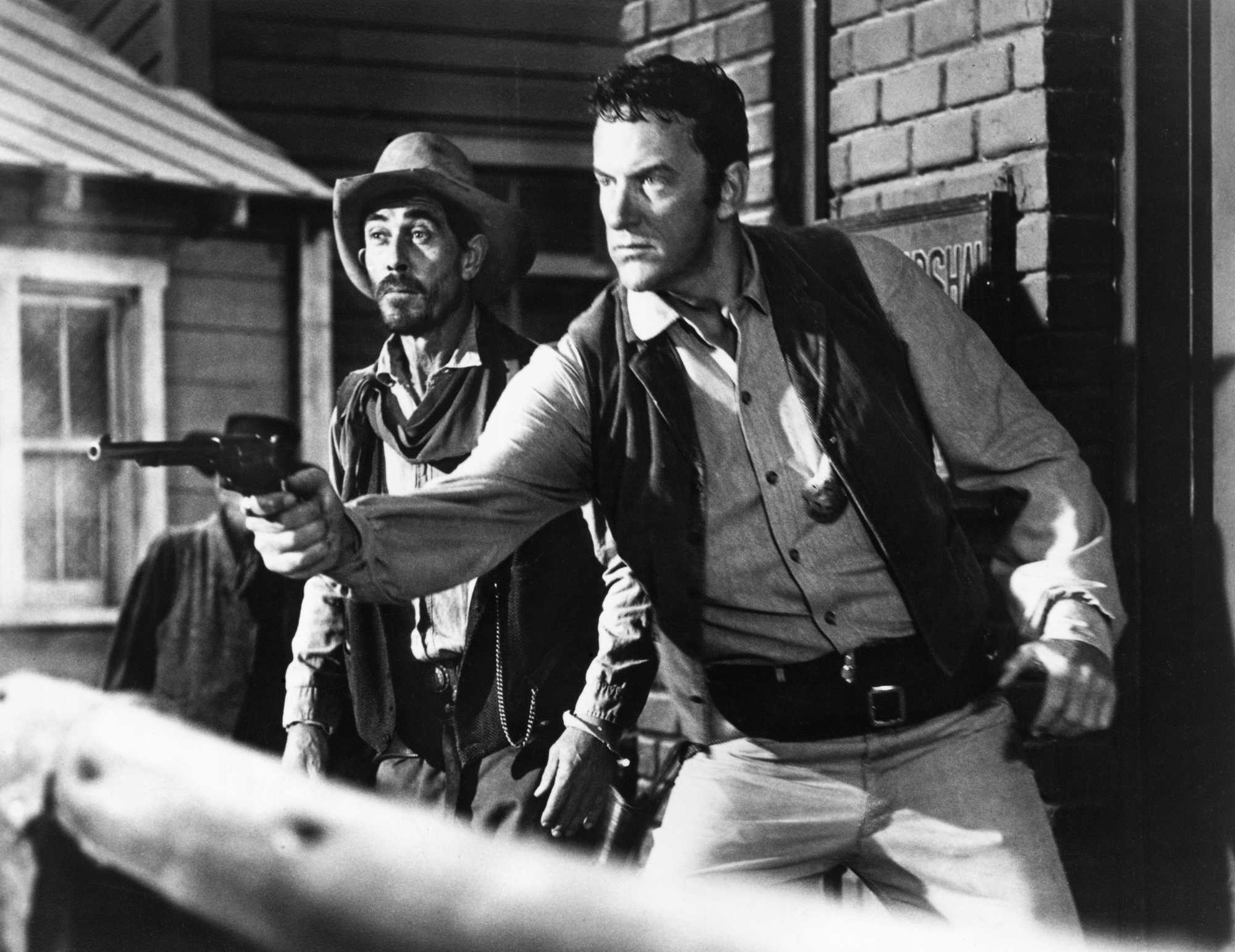 'Gunsmoke' Ken Curtis as Festus Haggen and James Arness as Matt Dillon with a gun. Matt is shooting his pistol and Festus is standing behind him looking surprised.