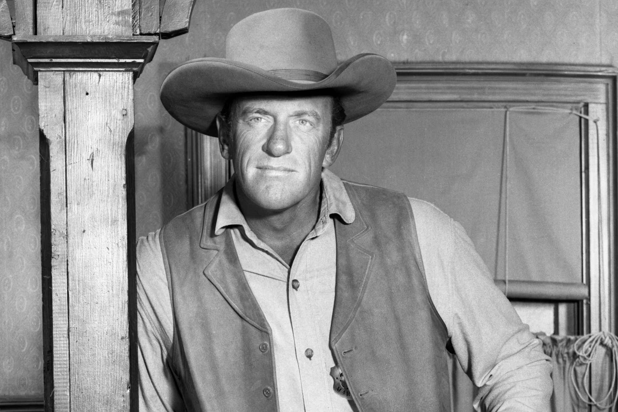 'Gunsmoke' episode James Arness as Matt Dillon leaning against a wooden beam, wearing a marshal costume.