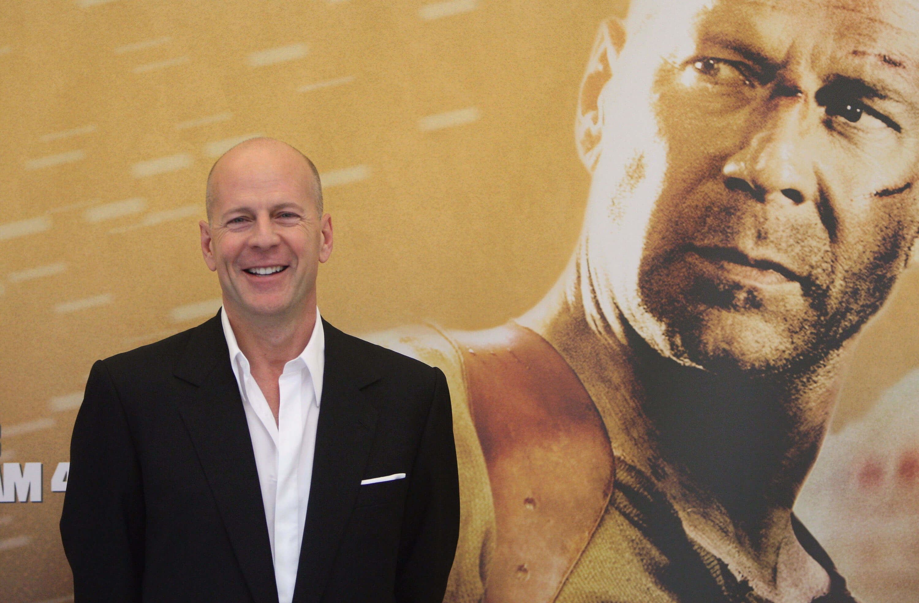 Bruce Willis poses in front of a 'Die Hard' movie poster.