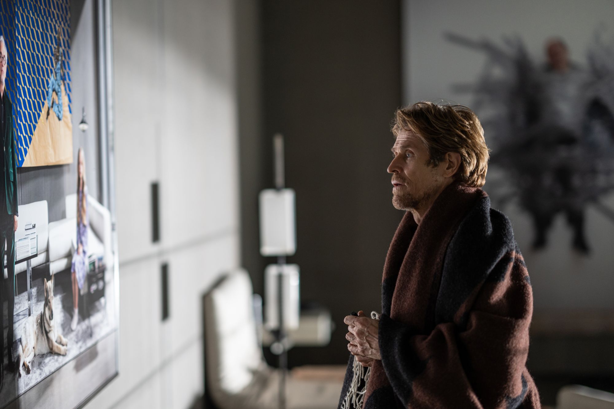 'Inside' Willem Dafoe as Nemo looking at a piece of art on the wall wrapped in a blanket.