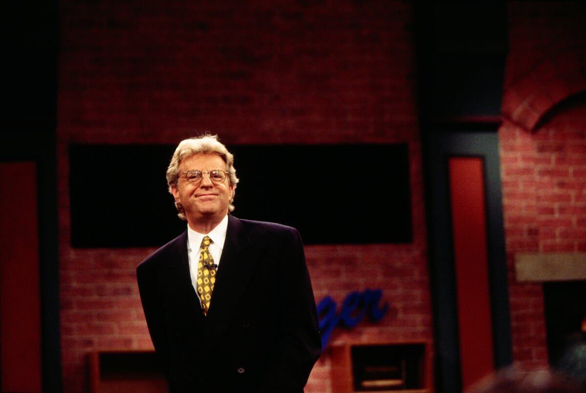 Jerry Springer standing on his show set in a suit
