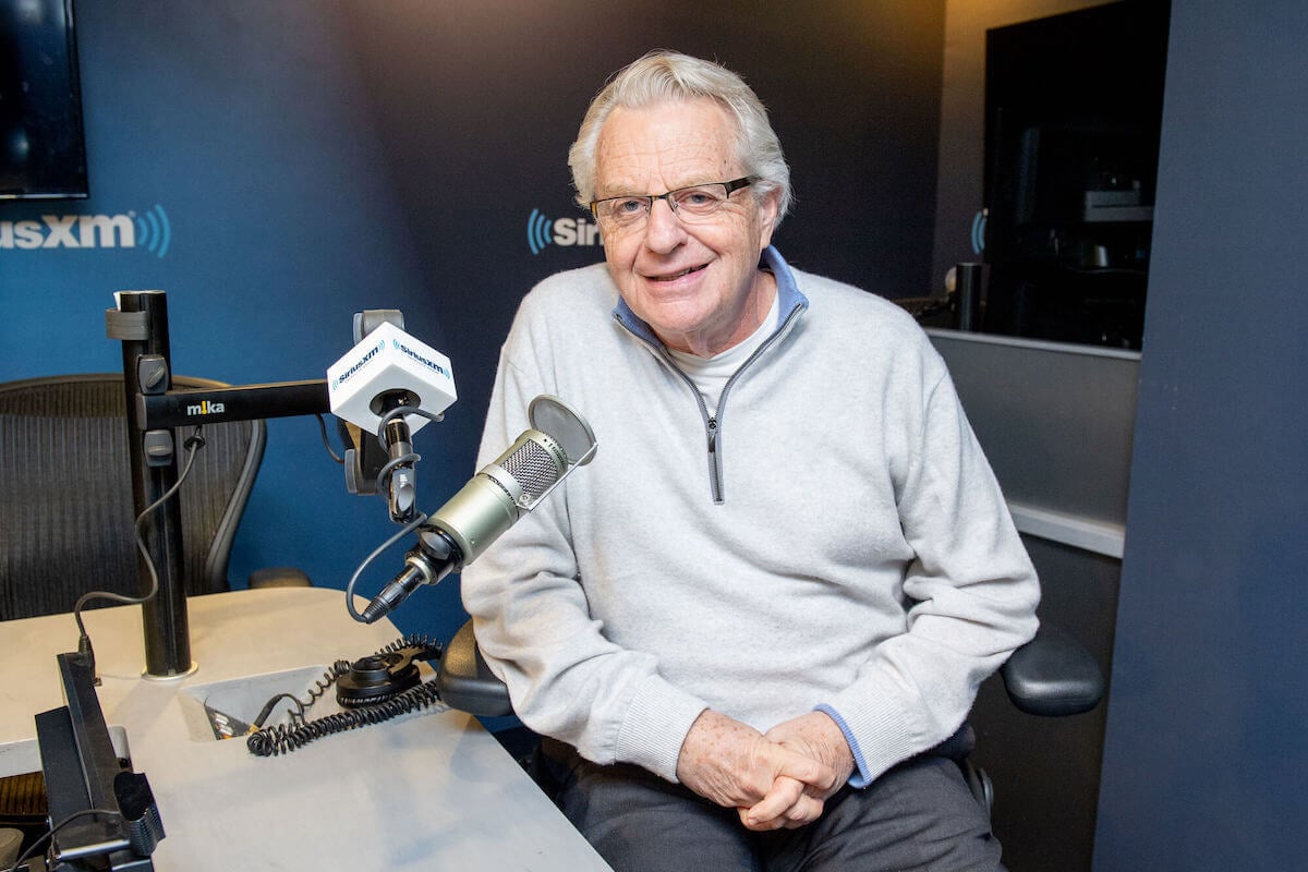 Jerry Springer smiling, sitting next to a microphone