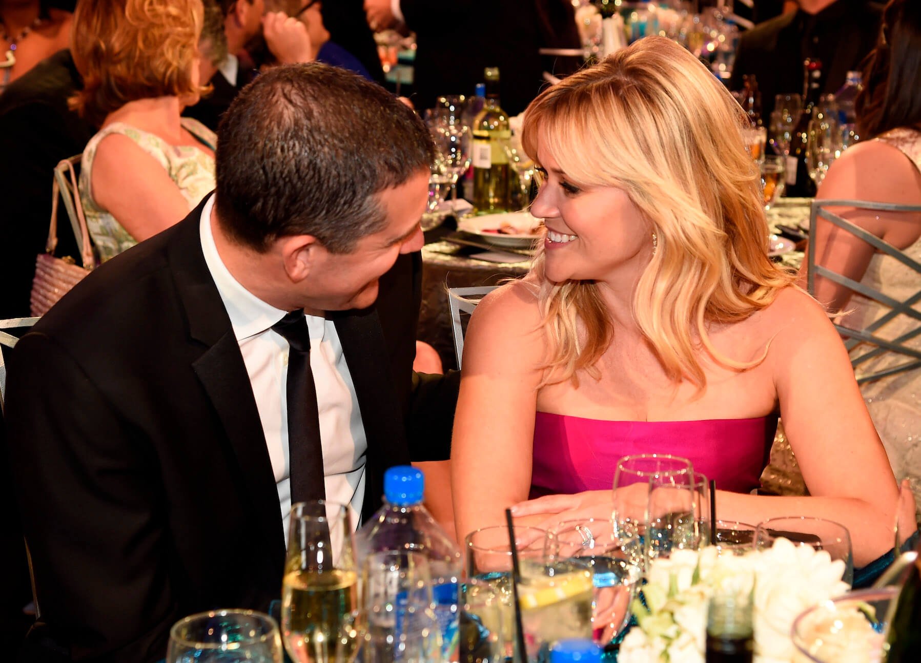 Jim Toth and Reese Witherspoon smiling at each other while sitting at an event. Witherspoon and Toth are getting a divorce in 2023.