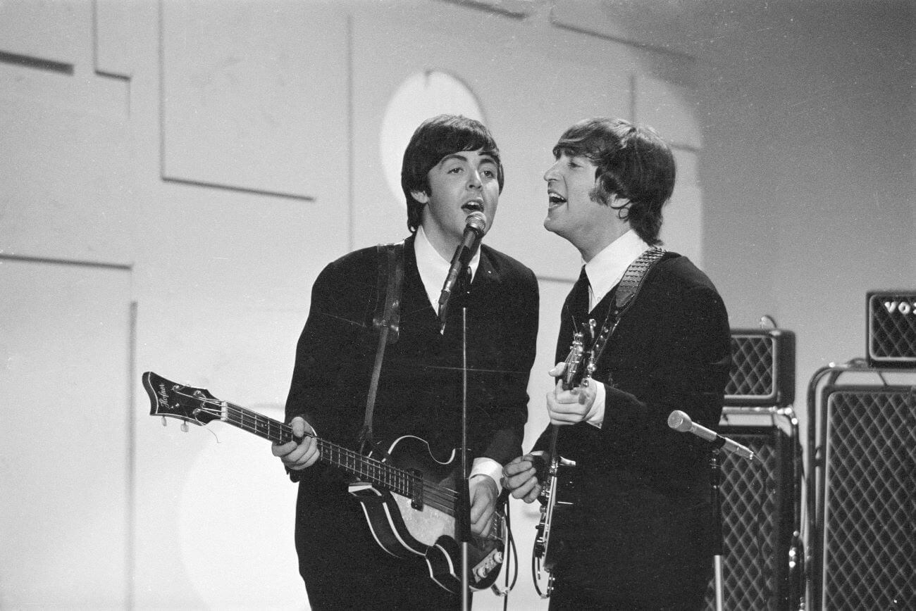 A black and white picture of Paul McCartney and John Lennon playing guitars and singing into the same microphone.