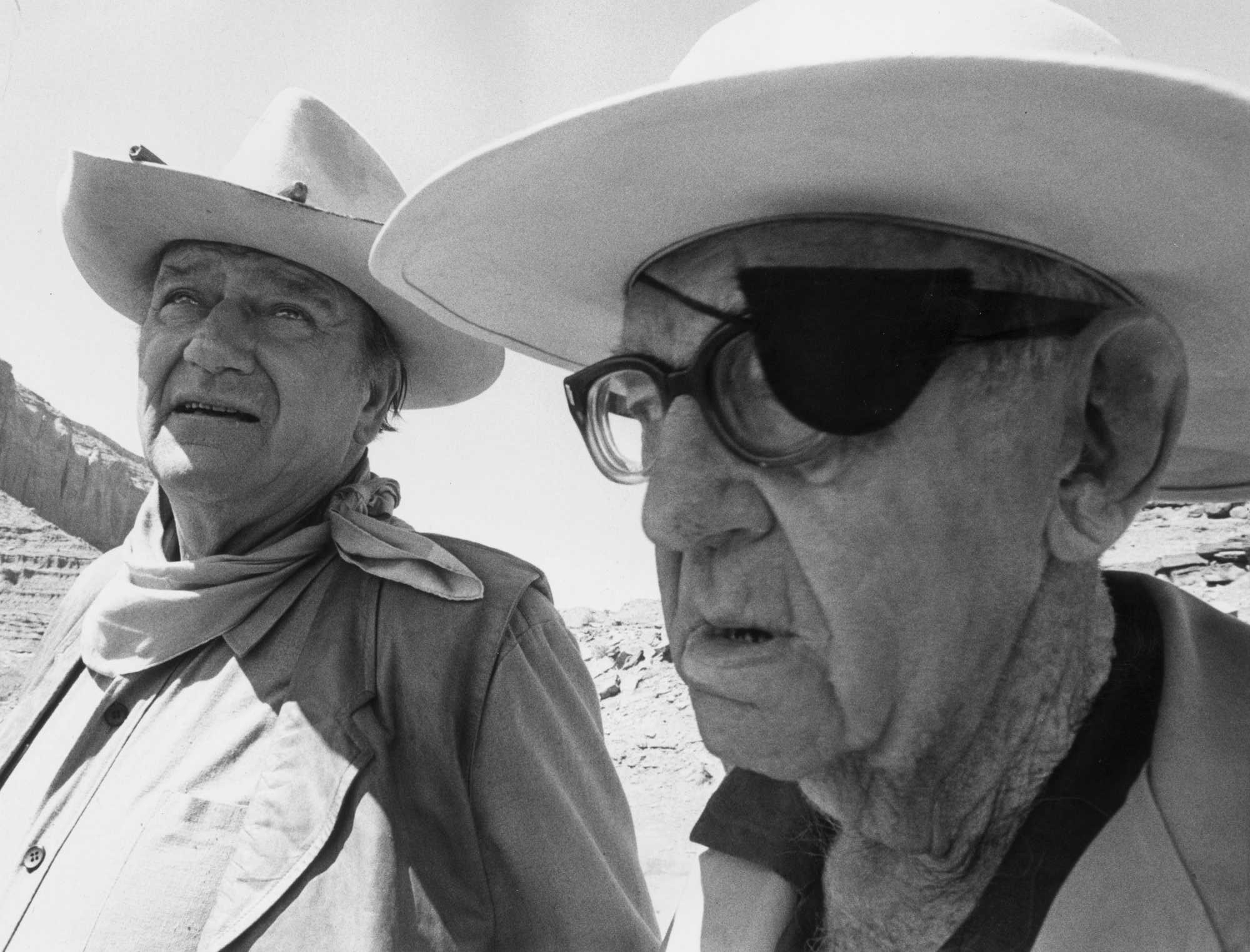 John Wayne and John Ford standing next to each other wearing cowboy hats, looking ahead.