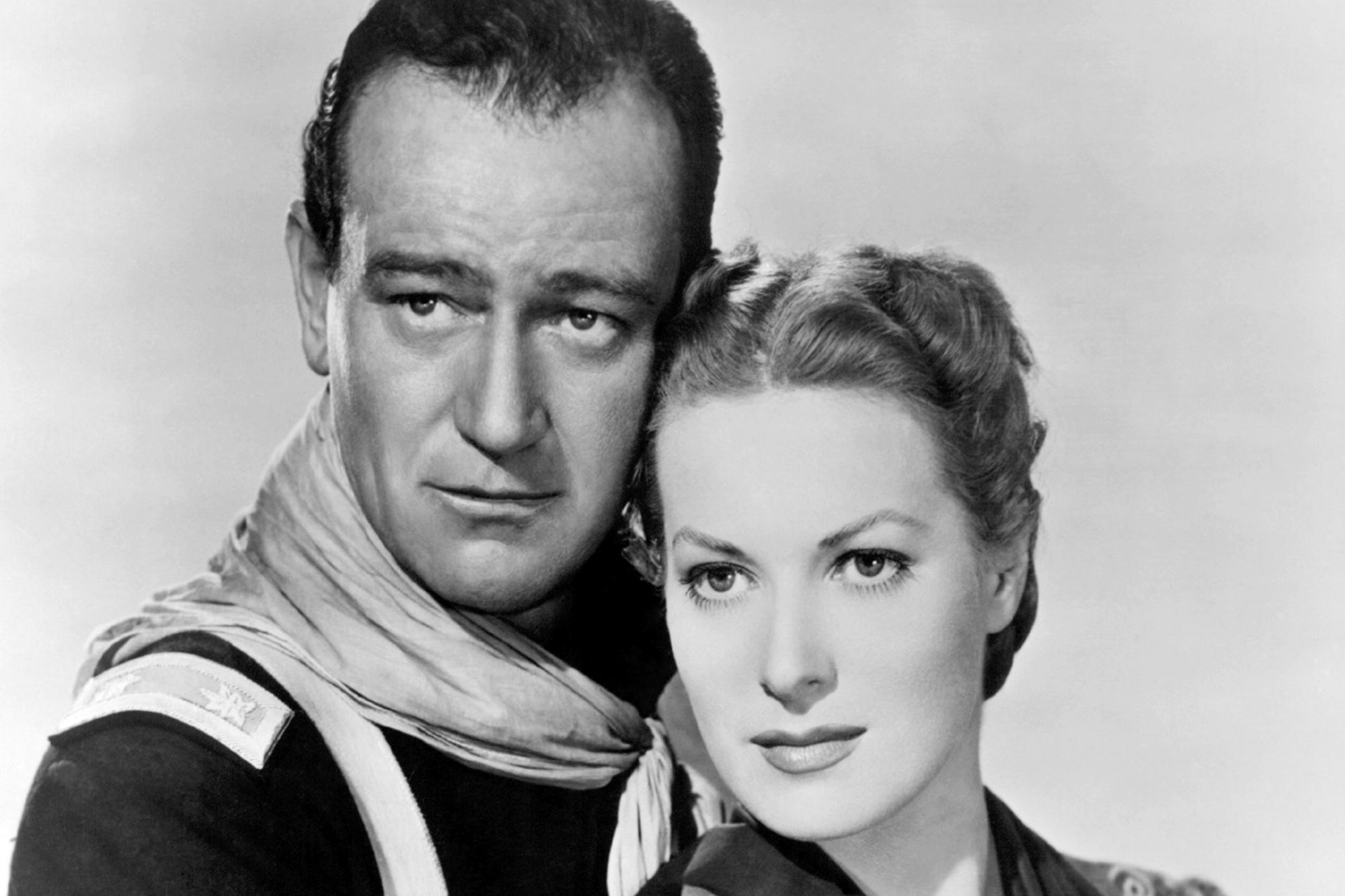 John Wayne and Maureen O'Hara in a black-and-white portrait with her head against his cheek, looking off to the side.