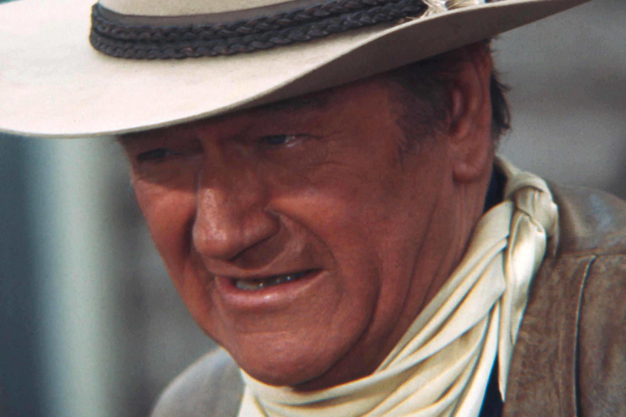 John Wayne, who starred in Western movies. He's wearing a cowboy hat, looking up from under the brim.