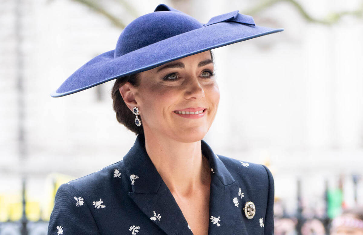 Kate Middleton smiling, wearing a navy floral suit