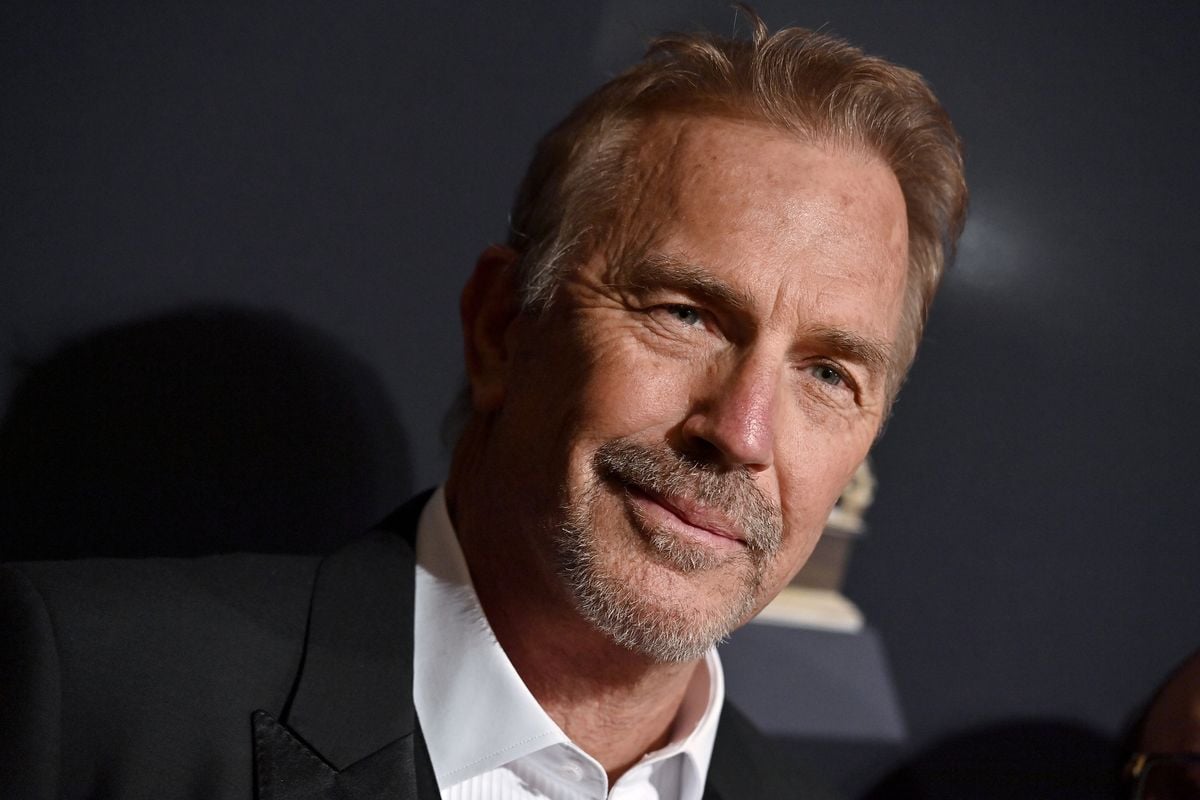 Kevin Costner poses in front of a black backdrop.