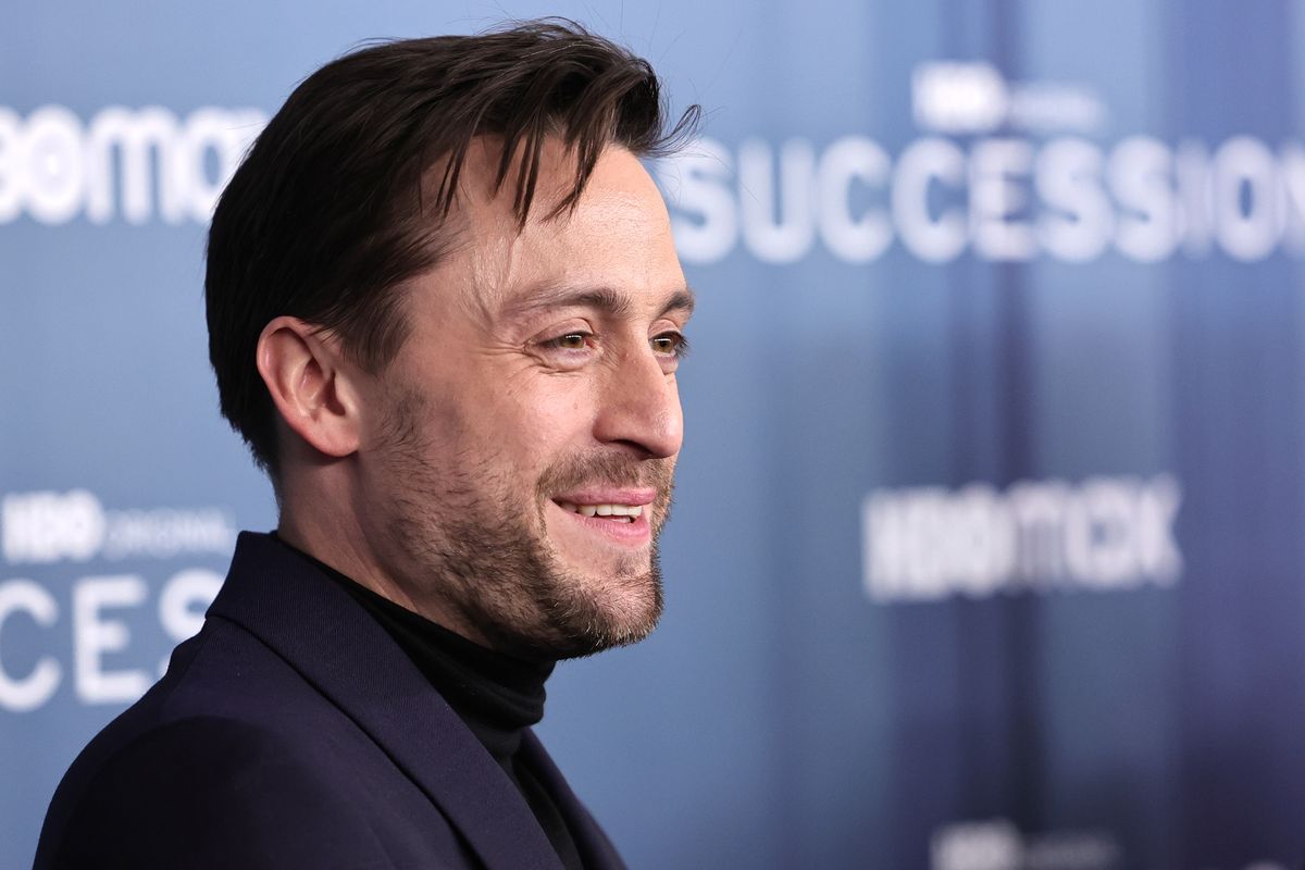 Kieran Culkin poses for photos in front of a backdrop featuring the "Succession" logo.
